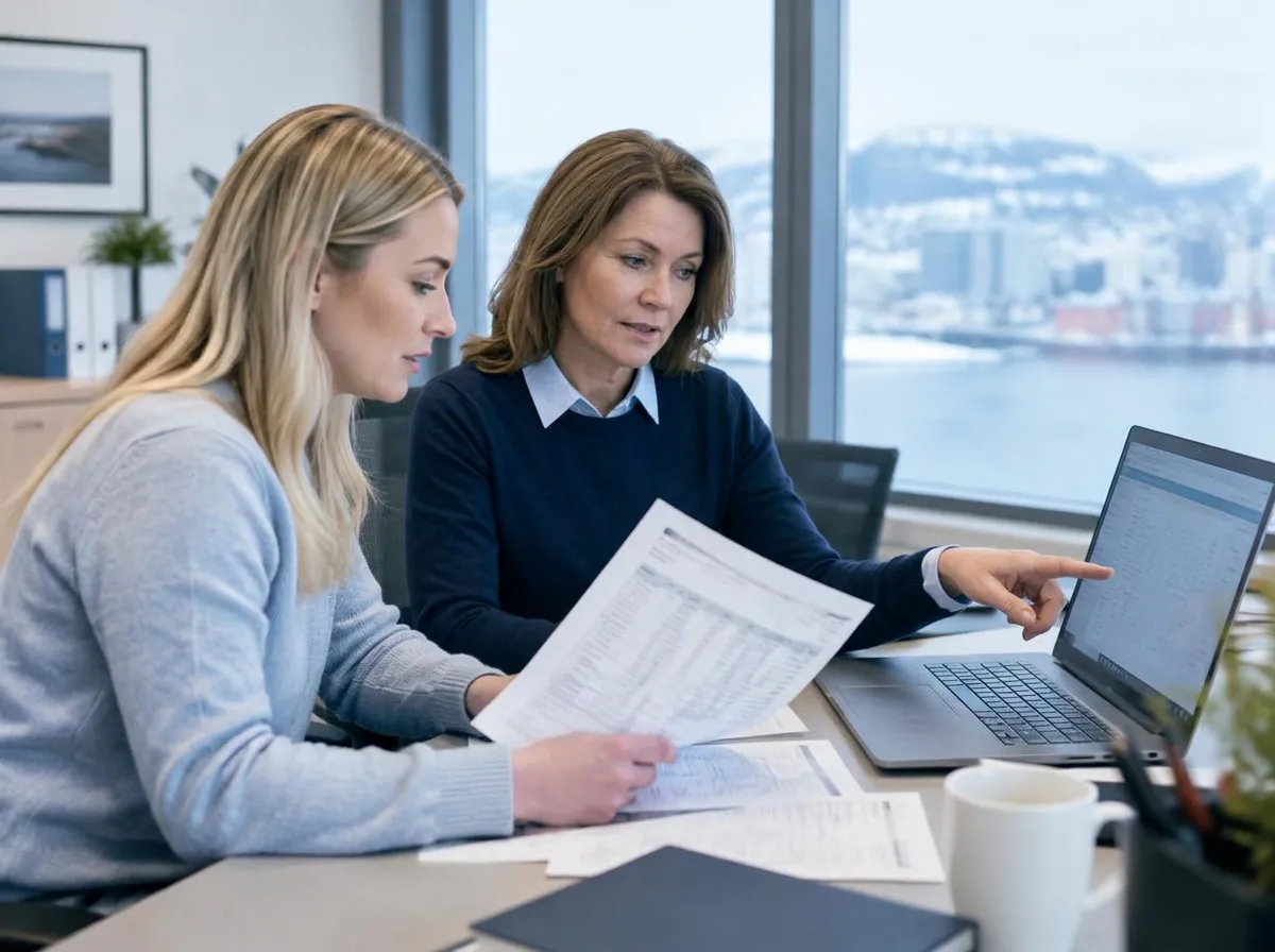 To kvinner ser på en utskrevet oversikt og en laptop ved et skrivebord med fjordutsikt